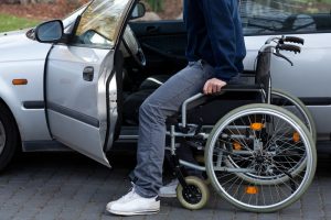 A man using a wheelchair transfers himself into a car.