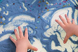 Art therapy with a child using blue sand and beads. Art therapy is an NDIS alternative therapy that can benefit children.