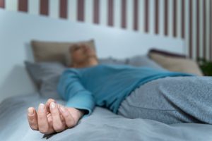 A person lying on a bed in a relaxed state, wearing a blue shirt and grey pants, suggesting a calm atmosphere conducive to meditations for sleep.