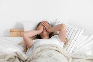 A woman in bed with hands covering her face, appearing stressed or unable to sleep, highlighting the potential need for meditations for sleep.