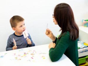 A boy engages in a speech therapy practice at home with a woman, using picture cards for exercises.