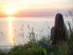 A woman reflecting by the water at sunset, considering a mental health risk assessment for personal wellbeing.