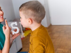 Child working on articulation disorders with therapist using a letter S for pronunciation practice.