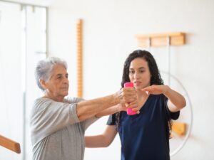 Senior woman receiving occupational therapy benefits through arm exercises guided by a therapist to improve mobility.