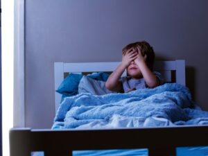 A boy covering his eyes in bed, experiencing fear, illustrating phobias in childhood.